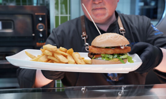 Ein Mitarbeiter des CID-Unternehmensrestaurants hält einen Teller mit Burger und Pommes Frites in der Hand